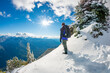 Adventurous male hiker standing on a mountain ridge in the snow looking out at the landscape.