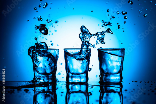 Strong alcoholic drink in dammed glasses with splashes on a blue background.
