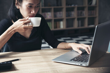 Wall Mural - Remote working at Home office Concept. Businesswoman working online via laptop and drink coffee. Asian young entrepreneur watching webinars and talking during meeting video conferences calls with team
