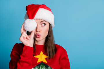 Poster - Portrait photo of young millennial girl wearing christmas cap keeping holding white soft cotton ball in hand looking at side with pouted plump lips sending air kiss isolated on blue color background