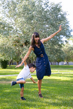 Excited Mom And Little Son Playing Active Games Outdoors, Standing And Balancing On One Leg, Doing Funny Exercises In Park. Family Outdoor Activity And Leisure Concept