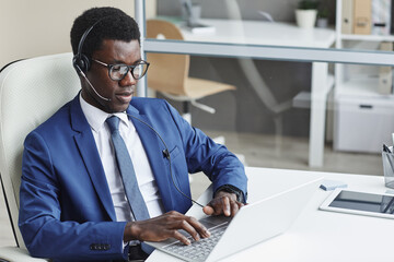 Wall Mural - African businessman in headphones typing on computer keyboard at his workplace at office