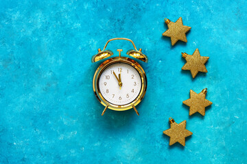 Golden alarm clock and gold stars on turquoise grunge background. Christmas and New Year composition. Top view, flat lay, copy space.