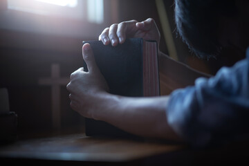 Wall Mural - Close up hands of youg male praying with holding the holy bible on wooden table in morning. Christian worship concept.
