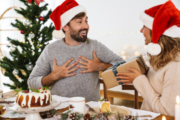 Wall Mural - Happy woman giving gift to his boyfriend while having Christmas dinner