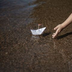 Wall Mural - child puts small paper boat on the water