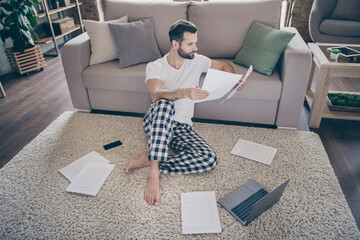 Canvas Print - Nice attractive focused guy agent broker manager sitting on carpet working remotely online reading analyzing finance law documents at modern loft industrial interior style flat indoors