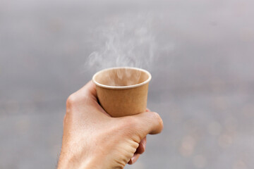 Hot cardboard cup with steaming drink in hand.
Heißer Kartonbecher mit dampfendem Getränk in der Hand.