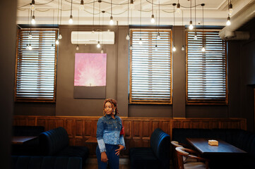 Wall Mural - Lovely african american woman with dreadlocks in blue stylish jeans jacket at cafe. Beautiful cool fashionable black young girl indoor.