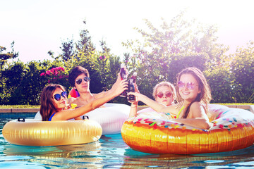 Wall Mural - Smiling boys and girls children sit in inflatable doughnut drinking soda in bottles with friends