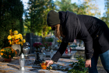 A woman wearing a protective mask against the coronavirus in the cemetery, holding a candle snitch in a hand. A woman in a cemetery during a pandemic. Covid on All Saints. Restrictions on the cemetery