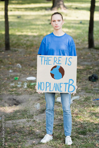woman looking at camera while holding placard with globe and there is no planet b inscription