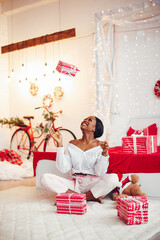 Beautiful girl in a decorated room. Woman near Christmas tree. Black lady in a white blouse