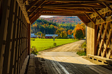 Looking From The Inside Of A Historic New England Covered Bridge Out At A Farm And Hills Covered In Fall Foliage Colored Trees
