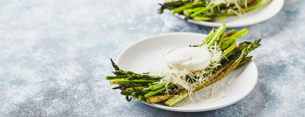 Wall Mural - Green asparagus with poached egg and parmesan, vegetarian breakfast served on white plate on light background.