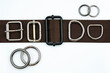 Brown belt with adjusters, buckles, rings, half rings top view. Metal bag accessories on a belt strap on a white background. Attachments for clothes and backpacks.