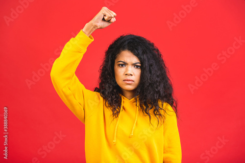 Angry brave African young woman isolated over red background raising fist and screaming. Mixed race lady activist feminist leader fight for women rights, gender equality, empowerment protest concept.