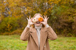© mdyn - The girl covers part of her face with an orange and white pumpkins. Harvest concept. Copy space. Autumn lifestyle. Smiling Woman being playful covering her eyes with pumpkins