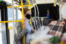 Teenage Girl Friends In Face Masks Talking On Public Bus