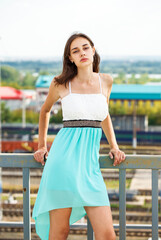 Wall Mural - Young beautiful woman in a luxurious turquoise dress posing on the street