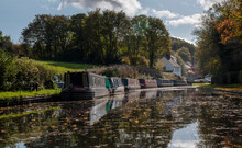 A Row Of Narrow Boats On One Of Dudley's Many Canals (or The Cut As We Know It) Near The Stewponey In Stourton. With Autumn Colours In The Trees And Still Reflective Water Bellow 