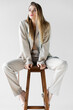 © LIGHTFIELD STUDIOS - trendy woman in suit sitting on wooden stool and looking away on white