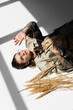 © LIGHTFIELD STUDIOS - high angle view of model in glasses, trench coat and scarf lying near wheat on white