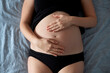 © Borislav Zhuykov/Westend61 - Pregnant woman touching stomach while lying on bed at home