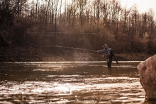 Man Throwing Fishing Reel In River To Catch Fish During Sunset