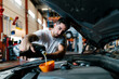© Ezequiel Gimenez/Westend61 - Auto mechanic filling engine oil while standing in garage
