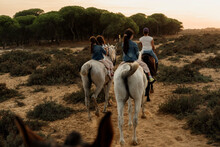 Mother With Daughters Riding Horses On Landscape Against Sky During Sunset