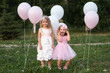 Little girls in pink and white dressses with balloons walking in the park