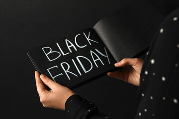 Woman holding notebook with words Black Friday on dark background, closeup