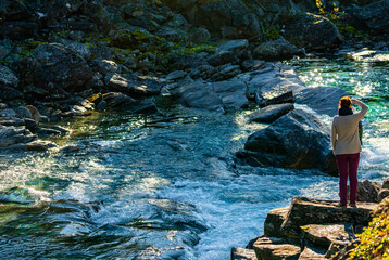 female hiker standing on a cliff by a wild river and waterfall enjoying the view.