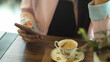 © bongkarn - Female hand holding smartphone with tea cup on wooden table in cafe