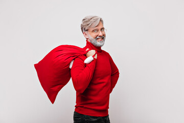 Handsome man with white beard celebrating new year. Carefree grandpa in red sweater posing with christmas presents.