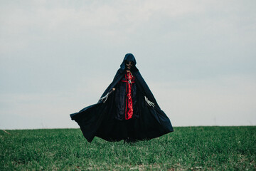 Wall Mural - Woman walks across field in Halloween costume of death against background sky.