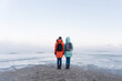 © Александр Коновалов - two girls in bright winter jackets do not admire the sweeping sea on the snowy shore beyond the Arctic Circle on a frosty winter day
