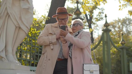 Wall Mural - Mature couple tourists standing near statue in park and reading information on cellphone