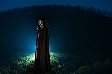 Wall Mural - Woman stands in Halloween costume of death against dark sky.