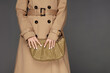 © Beauty Agent Studio - Female model posing against grey background dressed in trench coat and holding stylish bag. Autumn fashion concept