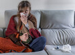 girl sitting on the sofa, covered with a colored blanket, with the flu and with a tissue to blow her snot