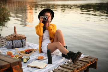 Wall Mural - Young woman taking picture with camera on pier at picnic