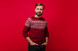 Confident white man with beard posing with hands in pockets. Studio shot of handsome guy with dark hair wears norwegian sweater.