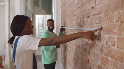 Side view of african couple measuring brick wall with tape