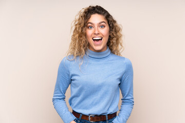 Young blonde woman with curly hair wearing a turtleneck sweater isolated on beige background with surprise facial expression