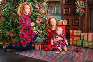 Red-haired curly children decorate Christmas tree in beautiful cozy interior.