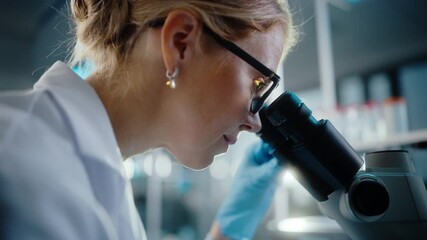 Wall Mural - in bright medical science laboratory: beautiful microbiologist wearing glasses looks under microscop