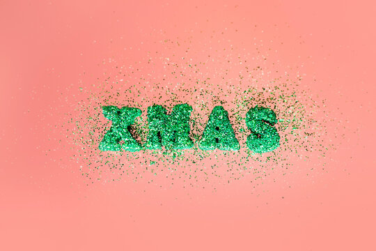 The letters in green sparkles are laid out in the word XMAS on a pink background. Minimalistic christmas concept.