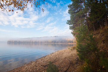 Wall Mural - autumn foggy morning on the river, bright colorful trees, fallen leaves and reflection of clouds in 